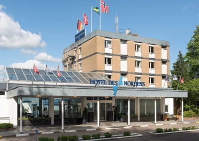 Außenansicht vom Hotel des Nordens mit überdachtem Eingangsbereich und Deutschland-Fahne, Dänemark-Fahne, Schweden-Fahne und Norwegen-Fahne auf dem Dach.