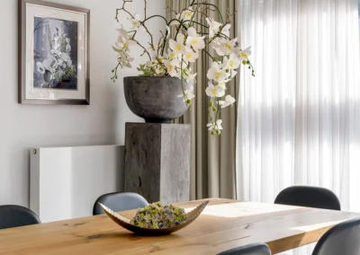 Esstisch mit Stühlen in einer Hotelsuite vor Fenster mit Gardine und Vorhang. Vor dem Vorhang steht eine große Orchidee auf einer Säule.