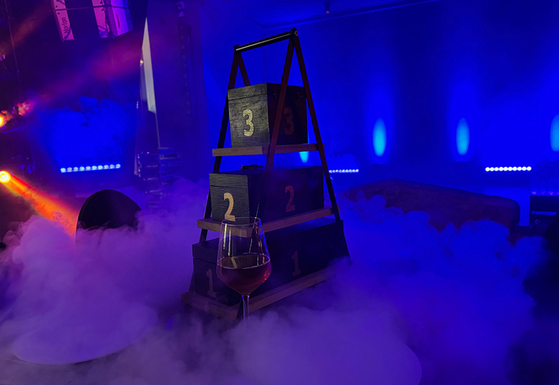 Blau beleuchterter Raum mit Nebel am Boden und einem 3-stufigem Gestell mit je einem Karton auf einer Stufe.